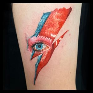 Get a stunning illustrative tattoo of David Bowie by artist Michaelle Fiore. Show your love for this legendary musician in style.