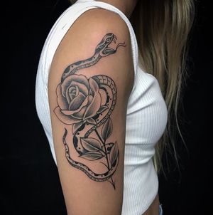 Get a striking blackwork and traditional tattoo featuring a snake and flower motif on your upper arm in sunny Miami.