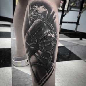 Detailed black-and-gray lower leg tattoo featuring a realistic woman and intricate rope design by Rico Dionichi.