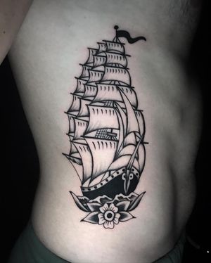 A stunning blackwork traditional tattoo on ribs by Chris Tambo, featuring a beautiful combination of flower and ship motifs.