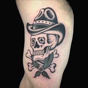 Unique blackwork tattoo on upper arm featuring skull, hat, and bones by artist Chris Tambo.