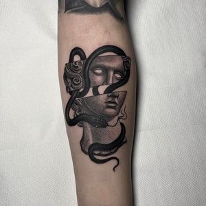 Get a stunning black and gray tattoo of a snake intertwined with a statue on your forearm in London, GB.