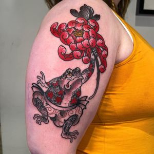 Get a stunning illustrative tattoo featuring a frog, chrysanthemum, and toad. Visit our London studio for this unique design!
