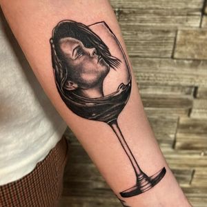 Elegant black and gray forearm tattoo featuring a woman with a wine glass, created by Michaelle Fiore.