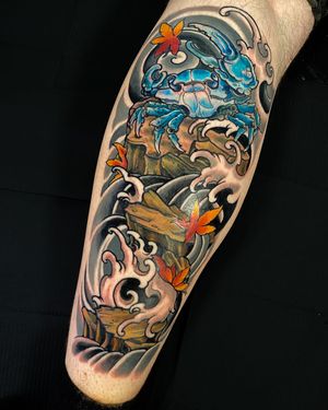 Stunning lower leg tattoo by Jethro Wood combines traditional Japanese elements of flowers, crabs, and waves in an illustrative style.