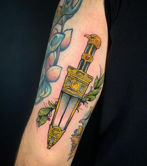 Intricate neo-traditional design on upper arm by artist Jethro Wood. Sword and leaf motifs blend beautifully in illustrative style.