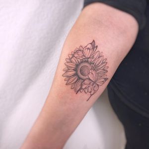 Beautiful forearm tattoo featuring a delicate butterfly and vibrant sunflower, designed by Polina in a fine line illustrative style.