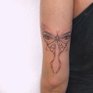Elegant fine line tattoo featuring a butterfly and eye motif, beautifully executed by Polina on the upper arm.