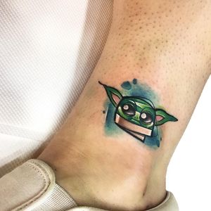 Get inked with a playful baby Yoda in new school style by tattoo artist Artemis. Vibrant colors and illustrative details make this ankle tattoo a standout piece.