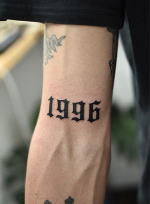 This stunning arm tattoo features bold blackwork lettering and illustrative elements representing the year 2022, expertly done by tattoo artist • ALEJANDRO •.