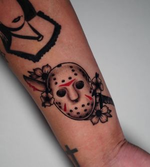 Unique illustrative tattoo by Miss Vampira, featuring a flower, mask, and knife design on the forearm in bold blackwork style.