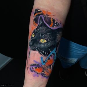 A stunning forearm tattoo by Marie Terry combining a realistic cat and butterfly in vibrant watercolor style.