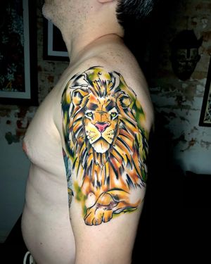 Express your wild side with this vibrant new school lion tattoo by artist Sandro Secchin on your upper arm.