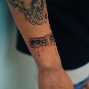 Detailed black and gray illustrative tattoo featuring a realistic eye shedding tears, done by Gabriele Edu.