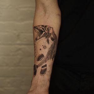 Gabriele Edu created a stunning black and gray tattoo featuring a fish skeleton in a geometric circle pattern on the forearm.