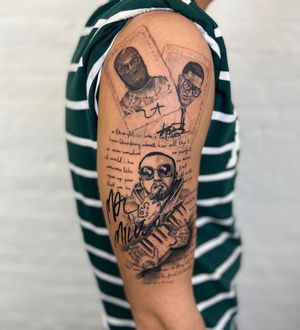 Illustrative tattoo of a man with glasses, a piano, rapper motif, and a meaningful quote on the upper arm. By Gabriele Edu.
