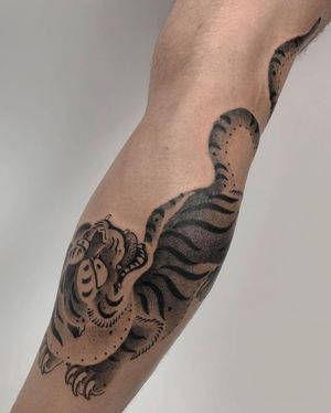 Get a fierce and detailed Japanese tiger tattoo on your lower leg by the talented artist FKM TATTOO. Embrace the power and beauty of this traditional motif in stunning blackwork style.