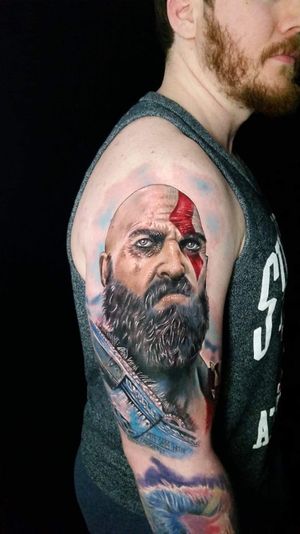 Incredible realism tattoo of the fierce warrior Kratos, expertly crafted on the upper arm by talented artist Marie Terry.