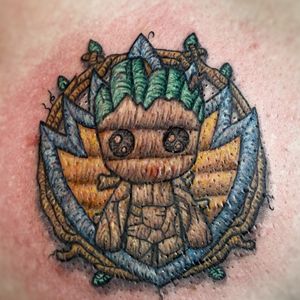 Embroidery style tattoo of baby Groot with the Guardians of the Galaxy badge and branches in the background. Much fun to be had with this style of tattoo. 🖤