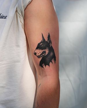 Jamie B showcases their blackwork skills with a stunning illustrative dog tattoo on the upper arm. A timeless piece of art for dog lovers.