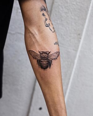 A striking blackwork bee tattoo on the forearm, expertly crafted by artist Jamie B. Bold and illustrative design.