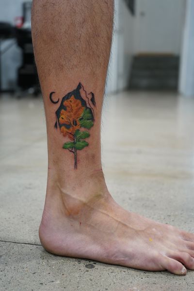 Elegant illustrative tattoo featuring a moon, mountain, tree, and flower design on the ankle. Perfect for nature lovers seeking a touch of celestial beauty.