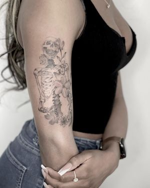 Elegant fine line illustration of a flower merging with a skeleton, expertly crafted on the upper arm by Lawrence.
