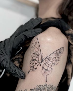 Transform your upper arm with Lawrence's intricate blackwork design featuring a stunning butterfly and delicate flower motif.