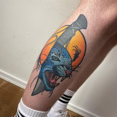 Get inked with this fierce and radiant tattoo on your lower leg by Sofia, featuring a vibrant sun, powerful leopard, and sharp dagger in neo-traditional style.