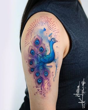 Striking watercolor peacock feather tattoo on the upper arm, showcasing the beauty and elegance of the majestic bird. By talented artist Houssam.