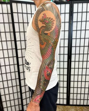 Get mesmerized by the exquisite fusion of a vibrant flower and majestic phoenix in this illustrative sleeve tattoo by Daniel Werder.