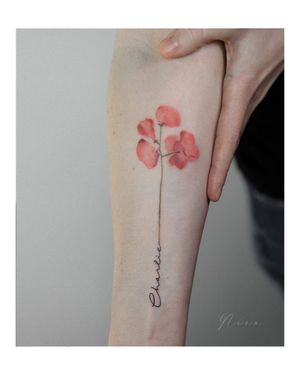 Beautifully designed tattoo on forearm by Nina featuring a vibrant watercolor flower and elegant lettering of a name.