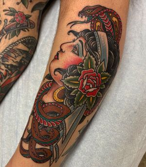 Stunning lower leg tattoo featuring a snake, flower, woman, and earrings in traditional style by Daniel Werder.