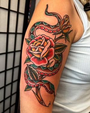 Beautiful traditional style tattoo featuring a snake and flower motif, expertly done by Andre Bertoncin on the upper arm.