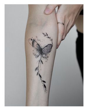 Elegant blackwork butterfly tattoo with intricate leaf design on forearm, created by talented artist Nina.