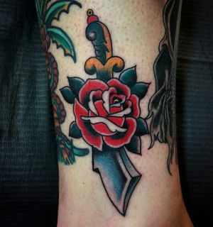 Beautiful traditional design by Arlene Salinas featuring a vibrant flower and menacing dagger on the ankle.