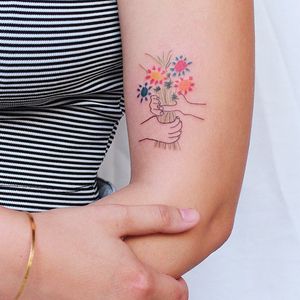Beautiful fine line tattoo of a flower and hand on the upper arm by Tuğçe özbıyık. A unique and delicate design.