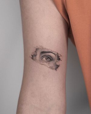 Detailed black and gray tattoo of a woman's eye on upper arm by Adrian Mokijewski. Unique and captivating design.