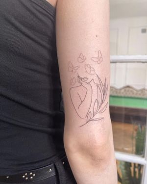 Beautiful and delicate upper arm tattoo featuring a fine line illustration of a butterfly, woman, and sprig by artist Dominika Gajewska.