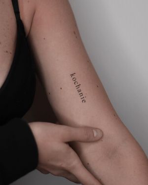 Get a unique and elegant upper arm tattoo featuring small lettering of your name and a meaningful quote by tattoo artist Adrian Mokijewski.