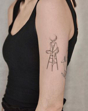 Adrian Mokijewski's illustrative black and gray tattoo features a beautiful woman sitting on a chair against a world background on the upper arm.