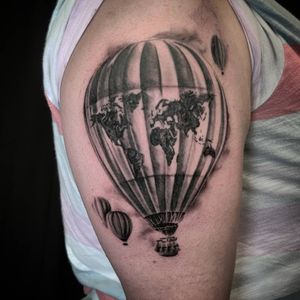Get a stunning blackwork and illustrative upper arm tattoo featuring a world map, hot air balloon, and Chicago skyline.