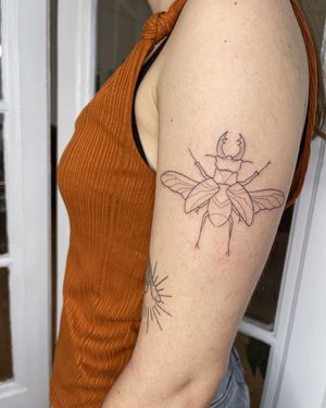 Get a beautifully detailed beetle design on your upper arm with this illustrative, fine line tattoo by Dominika Gajewska.