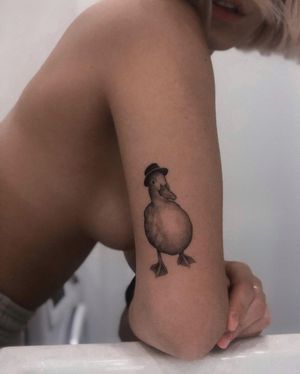 Admire the detailed blackwork of a duck wearing a hat on your upper arm by artist Adrian Mokijewski.