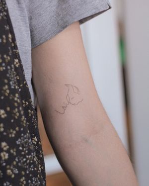Elegant upper arm tattoo featuring a minimalist cat intertwined with a graceful woman, done by Dominika Gajewska.