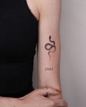 Adrian Mokijewski's blackwork snake tattoo with intricate lettering and illustrative elements on upper arm.