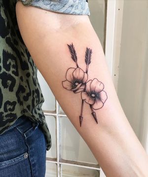 Bold blackwork design by Natalie Lucia, featuring a stunning floral motif intertwined with a sleek arrow on the forearm.