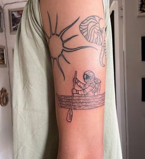 Elegant blackwork illustration on upper arm by Natalie Lucia, featuring an astronaut and a boat in a fine line style.
