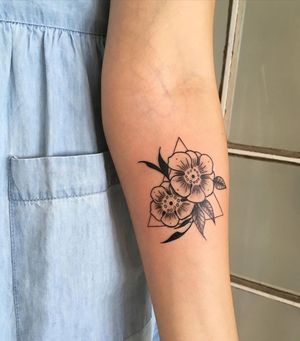 A bold blackwork forearm tattoo featuring a geometric triangle intertwined with a delicate flower, expertly done by artist Natalie Lucia.