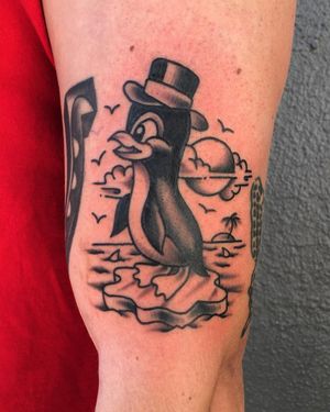 Beautiful blackwork upper arm tattoo featuring a sun, bird, tree, penguin, hat, and ice by Phil Botha.